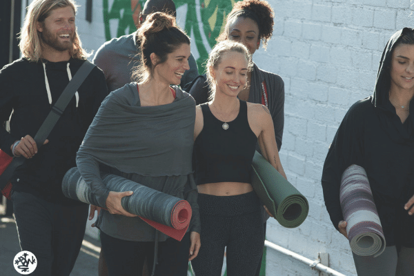 group of yoga students smiling with yoga mats in hand